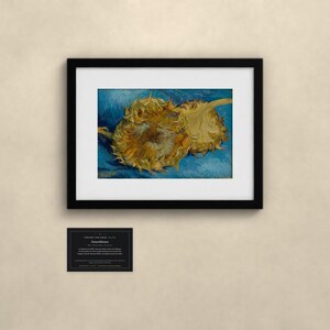 May include: A framed print of Vincent van Gogh's Sunflowers painting, featuring two golden-yellow sunflowers against a textured blue background. Below the black frame is a small rectangular plaque with white text detailing the artwork.
