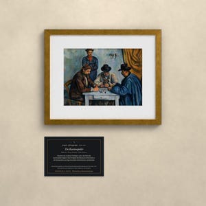 May include: A framed art print of Paul C&eacute;zanne's The Card Players, depicting four figures seated at a table playing cards. Below the gold-framed print is a black informational plaque with white text detailing the artwork's history and provenance.