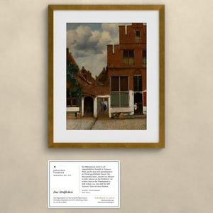 May include: A framed print of Johannes Vermeer's painting The Little Street, featuring red brick houses, a cobblestone path, and a cloudy sky. Below the frame is a white information card with black text detailing the artwork's history.