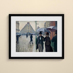 May include: A framed art print of a painting depicting a rainy Parisian street scene with cobblestones, tall buildings, and figures walking with umbrellas. A couple in formal attire stands in the foreground under a large grey umbrella.