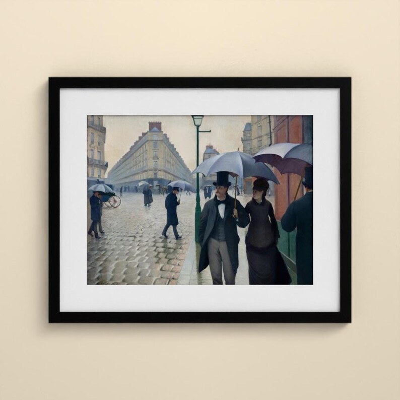 May include: A framed art print of a painting depicting a rainy Parisian street scene with cobblestones, tall buildings, and figures walking with umbrellas. A couple in formal attire stands in the foreground under a large grey umbrella.
