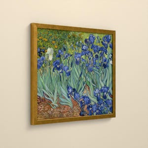 May include: A framed art print featuring a painting of blue irises with green stems and leaves, set against a background of orange and yellow flowers and brown earth, enclosed in a simple gold-colored frame.