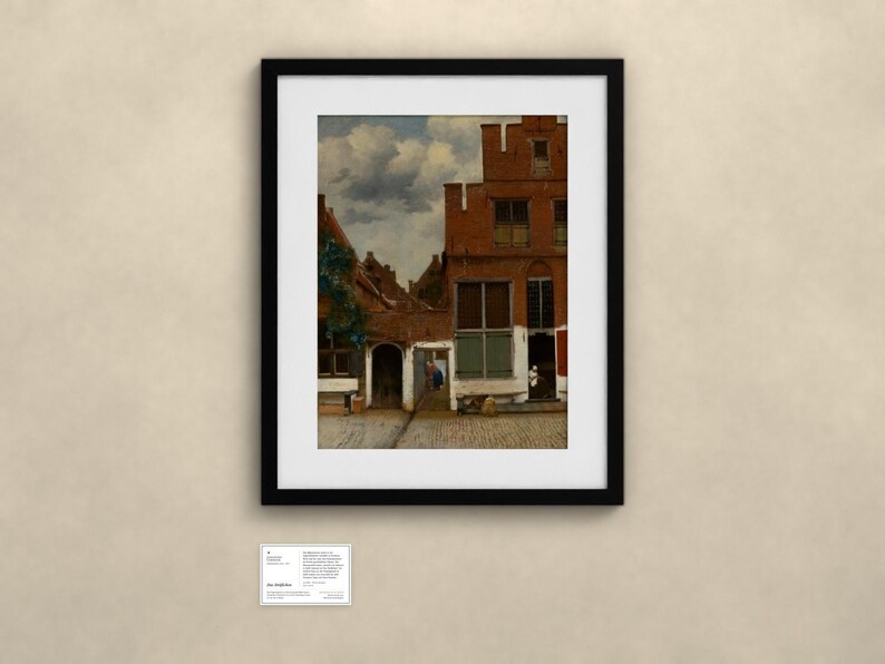 May include: A framed art print depicting a Dutch street scene with red brick buildings, a cobblestone path, and a cloudy sky. Below the frame, a small white informational card is displayed with the text The Little Street.