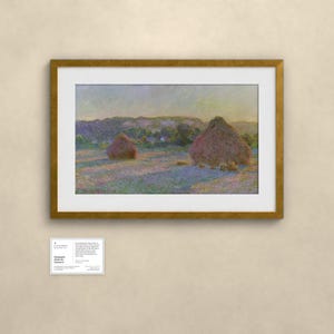 May include: A framed landscape painting featuring two large haystacks in a field under a soft, hazy sky. The artwork uses impressionistic brushstrokes in shades of gold, purple, and green. Below the frame is a small white informational card.