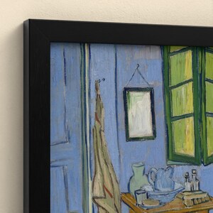 May include: A framed print of a painting featuring a blue interior room with a green window, a hanging cloth, a small framed picture on the wall, and a wooden table holding a blue pitcher, a bowl, and small glass bottles.