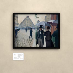 May include: A framed print of Gustave Caillebotte's Paris Street; Rainy Day, depicting figures with umbrellas walking on a cobblestone street in front of tall buildings. A small white informational plaque is mounted below the framed artwork.
