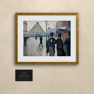 May include: A framed print of the painting Paris Street; Rainy Day, featuring figures in formal attire with umbrellas walking on a cobblestone street. The artwork is displayed in a gold frame with a white mat, accompanied by a small black plaque.