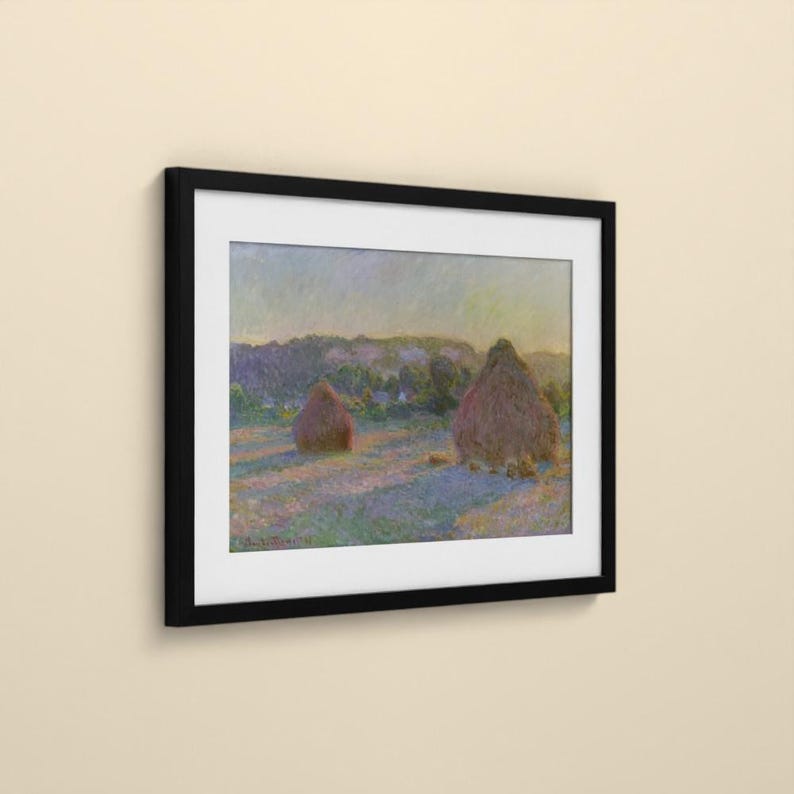 May include: A framed art print featuring an impressionist landscape painting of two haystacks in a field. The scene displays soft hues of purple, blue, and yellow under a pale sky. The artwork is enclosed in a simple, solid black rectangular frame.