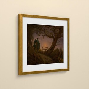 May include: A framed art print featuring a dark, atmospheric landscape painting of two figures standing under a large, gnarled tree at twilight. A thin crescent moon is visible in the sky. The artwork is enclosed in a square gold frame with a white mat.