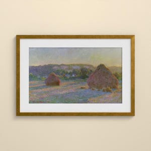 May include: A framed landscape painting featuring two large haystacks in a field under a soft sky. The artwork uses a palette of muted purples, blues, and golden yellows to depict the scene, enclosed in a metallic gold frame with a white mat.