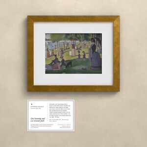 May include: A framed print of Georges Seurat's painting A Sunday on La Grande Jatte, featuring figures in a park by the water. Below the gold-framed artwork is a white informational card with the text Georges Seurat, Ein Sonntag auf La Grande Jatte.