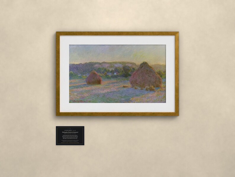 May include: A framed art print featuring an impressionist landscape painting of two haystacks in a field at sunset. The scene displays soft purple and gold light across the grass, with a small black informational plaque mounted below the frame.