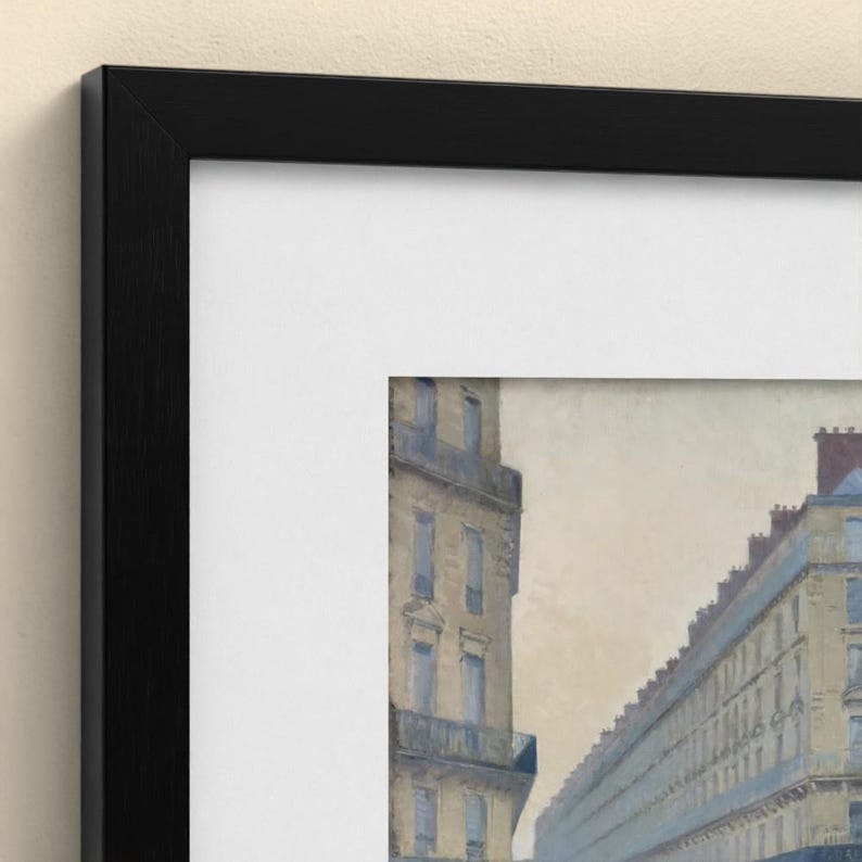 May include: A framed print featuring a painting of a city street scene with tall, multi-storey buildings in muted beige and blue tones. The artwork is encased in a wide white mount and a thin, black wooden frame with a visible wood grain texture.
