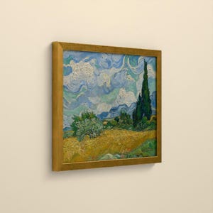 May include: A framed landscape painting featuring a golden wheat field under a swirling blue and white sky. A tall, dark green cypress tree stands on the right side, while a smaller green tree sits in the middle of the field.