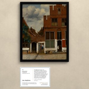 Op de afbeelding: Een ingelijste print van Johannes Vermeer's schilderij Het Straatje, met een rood bakstenen huis, een kasseienpad, een bewolkte lucht en figuren in deuropeningen. Onder de lijst bevindt zich een informatiekaart met Duitse tekst.
