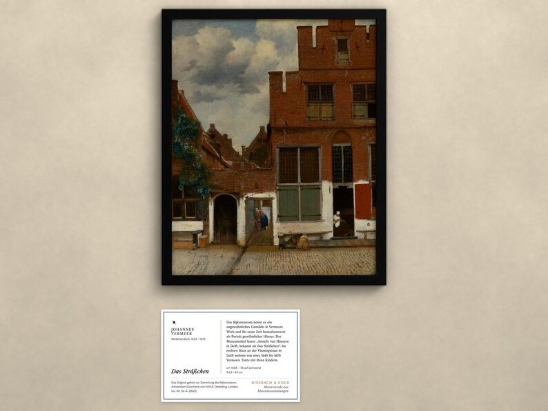 Op de afbeelding: Een ingelijste print van Johannes Vermeer's schilderij Het Straatje, met een rood bakstenen huis, een kasseienpad, een bewolkte lucht en figuren in deuropeningen. Onder de lijst bevindt zich een informatiekaart met Duitse tekst.
