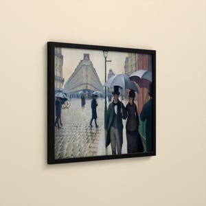 May include: A framed print of an oil painting depicting a cobblestone street in Paris on a rainy day. People in formal attire carry umbrellas while walking past tall buildings. A man and a woman stand in the foreground under a large umbrella.