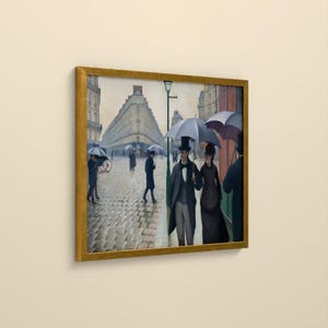 May include: A framed print of a painting depicting a cobblestone street scene in Paris on a rainy day. People in formal attire carry umbrellas while walking past tall buildings. A man in a top hat and a woman in a dark dress walk together in the foreground.