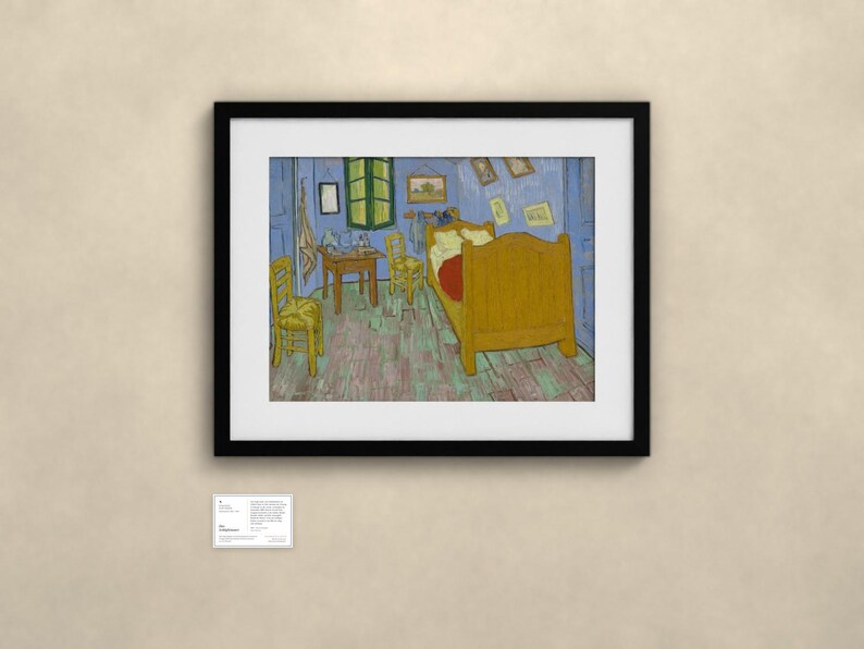 May include: A framed print of Vincent van Gogh's Bedroom in Arles painting, featuring a yellow bed, two yellow chairs, a wooden table, and blue walls, displayed in a black frame with a small informational plaque mounted below it.