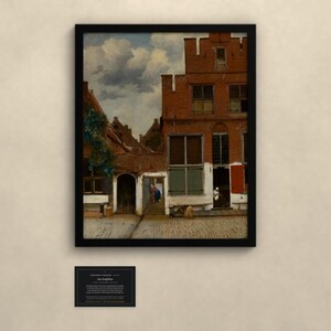 May include: A framed art print of a Dutch cityscape featuring red brick buildings with stepped gables, a cobblestone courtyard, and a cloudy sky. The painting depicts architectural details including windows, a dark arched doorway, and a small figure near the entrance. A black plaque with white text is positioned below the framed artwork.