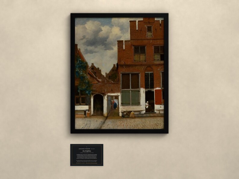 May include: A framed art print of a Dutch cityscape featuring red brick buildings with stepped gables, a cobblestone courtyard, and a cloudy sky. The painting depicts architectural details including windows, a dark arched doorway, and a small figure near the entrance. A black plaque with white text is positioned below the framed artwork.