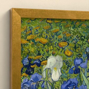 May include: A framed painting featuring a field of vibrant yellow flowers and deep blue and white irises. The artwork is enclosed in a metallic gold frame with a clean, angular profile, showcasing thick, textured brushstrokes throughout.