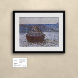 K&ouml;nnte beinhalten: Ein gerahmter Druck von Claude Monets Gem&auml;lde "Haystacks in Snow" mit einem dunkelbraunen Heuhaufen auf einem verschneiten Feld, im Hintergrund B&auml;ume und Berge in Blaut&ouml;nen. Unter dem Rahmen befindet sich eine kleine Informationskarte.