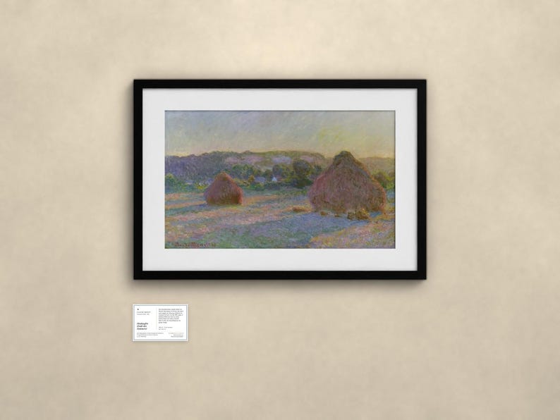 May include: A framed landscape painting featuring two large haystacks in a field under a soft sky. The artwork displays muted tones of yellow, purple, and green. Below the frame, a small white informational placard contains printed text.