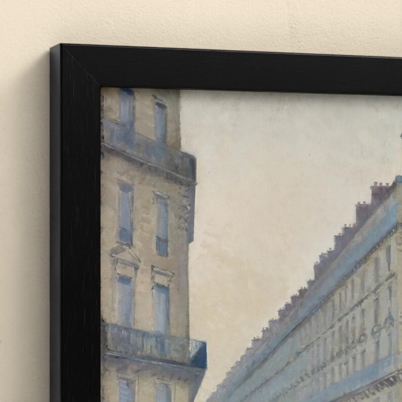 May include: A framed painting depicting a city street scene with tall, multi-story buildings in muted beige and blue tones. The artwork is enclosed in a simple, solid black frame, showcasing architectural details like windows and balconies.