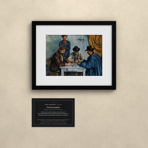 May include: A framed art print of Paul C&eacute;zanne's The Card Players, depicting three men in hats playing cards at a table, with a standing figure behind them. Below the frame is a black informational plaque with white text detailing the artwork.