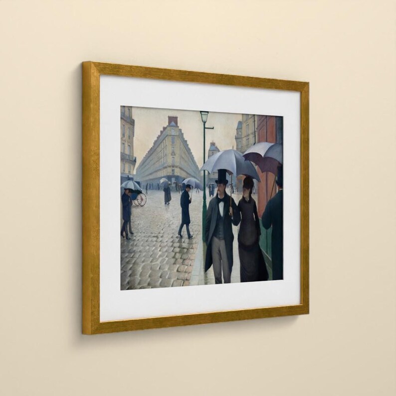 May include: A framed print of a painting depicting a cobblestone street scene in Paris. Figures in formal attire carry umbrellas under a grey sky. The artwork is encased in a gold-toned frame with a white mat, showcasing a classic urban setting.