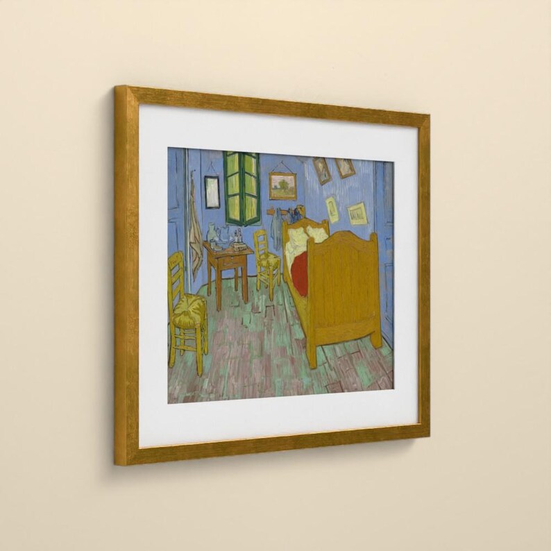 May include: A framed art print depicting a bedroom scene with a wooden bed, two chairs, and a small table. The room features blue walls, a light-colored floor, and several small framed pictures hanging on the wall. The frame is gold-toned.