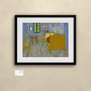 May include: A framed art print of Vincent van Gogh's Bedroom in Arles, featuring a yellow bed, two yellow chairs, a wooden table, and blue walls, displayed in a black frame with a white mat and a small informational plaque below it.