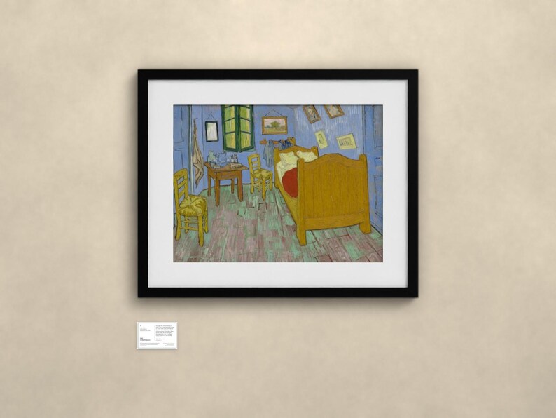 May include: A framed art print of Vincent van Gogh's Bedroom in Arles, featuring a yellow bed, two yellow chairs, a wooden table, and blue walls, displayed in a black frame with a white mat and a small informational plaque below it.