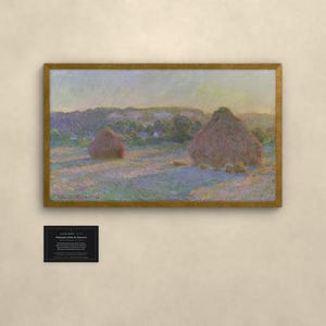 May include: A framed landscape painting featuring two large haystacks in a field under a soft sky, with visible brushstrokes in shades of purple, gold, and green. Below the painting is a small black plaque with white text detailing the artwork.