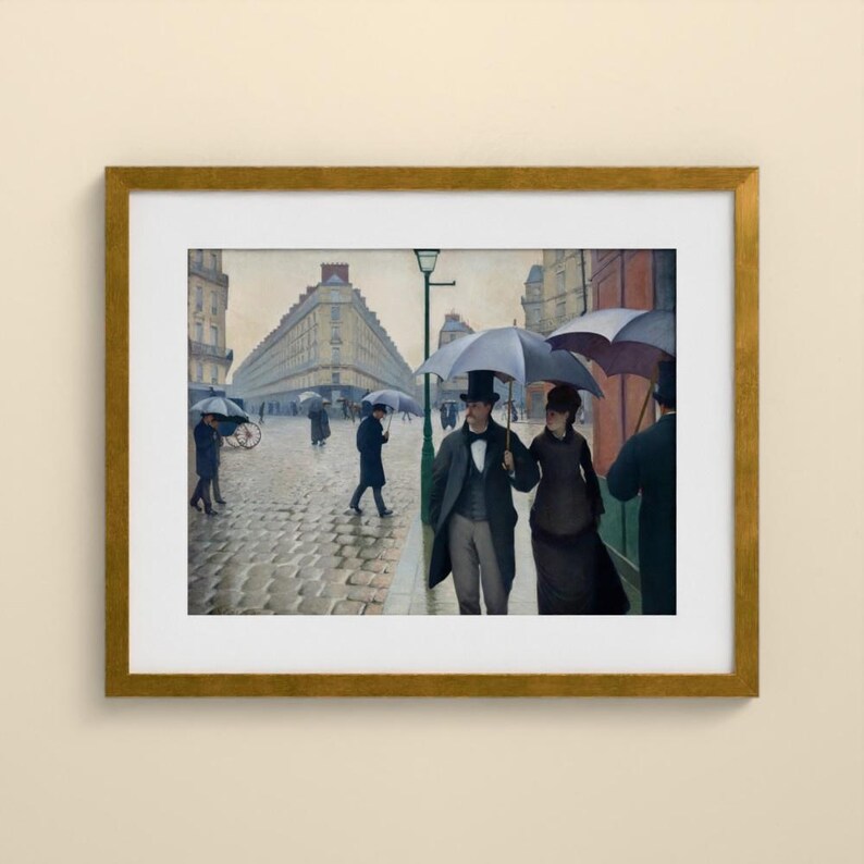 May include: A framed print of a painting depicting a rainy Parisian street scene with cobblestones, tall buildings, and people walking with umbrellas. A couple in the foreground wears dark coats and hats, while others walk in the distance.