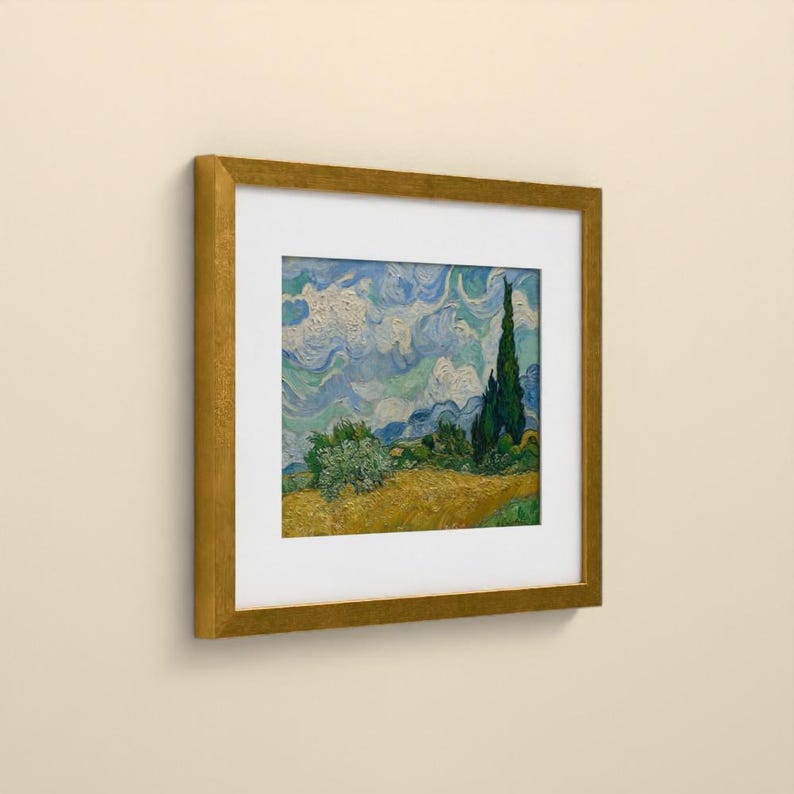 May include: A framed print of a landscape painting featuring a golden wheat field, a dark green cypress tree, and a swirling blue and white sky. The artwork is enclosed in a square, metallic gold frame with a wide white mat border.