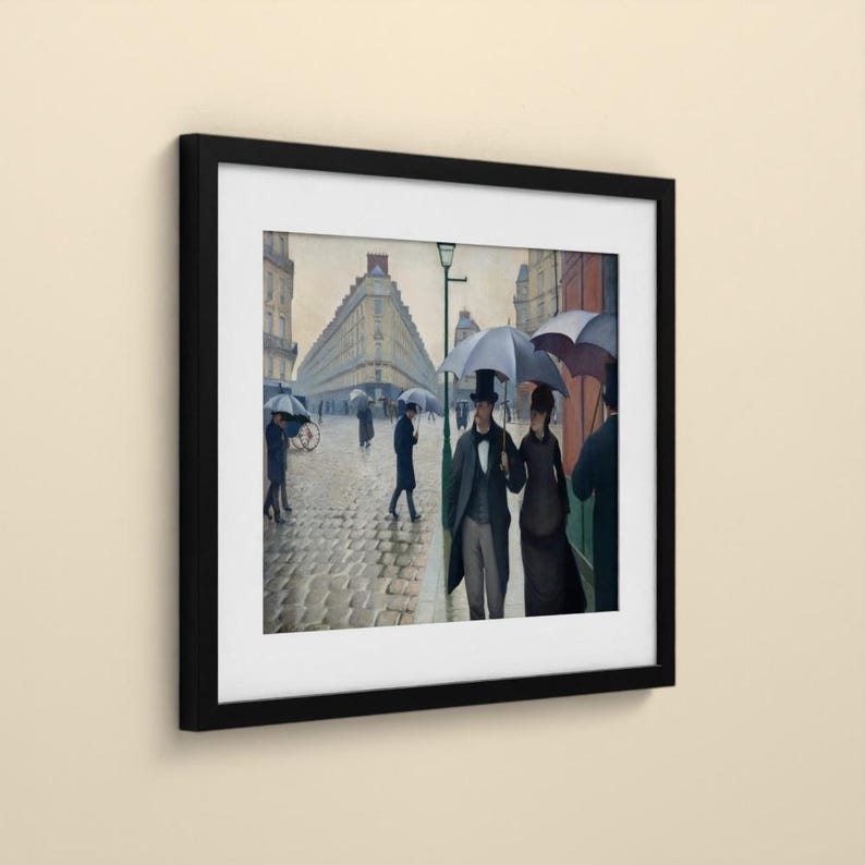 May include: A framed print of a painting depicting a rainy Parisian street scene with cobblestones, featuring figures in dark coats and top hats carrying umbrellas, set against tall buildings under a muted, overcast sky.