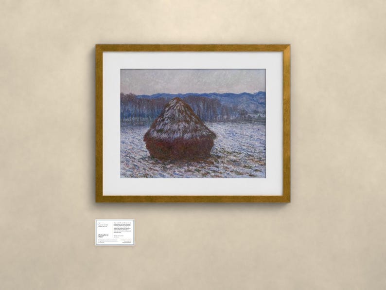 May include: A framed landscape painting featuring a dark brown haystack in a snow-covered field under a pale sky, with blue-toned hills in the distance. A small white informational placard is positioned below the gold-toned frame.