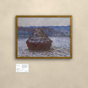 May include: A framed landscape painting featuring a large, dark brown haystack centered in a snowy field. The background displays blue-toned trees and distant mountains under a pale sky. A small white informational placard is positioned below the frame.