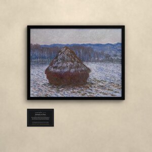 May include: A framed print of Claude Monet's Haystacks in Winter, featuring a dark brown haystack in a snow-covered field with blue-toned trees and mountains in the background. A small black informational plaque is mounted below the framed artwork.