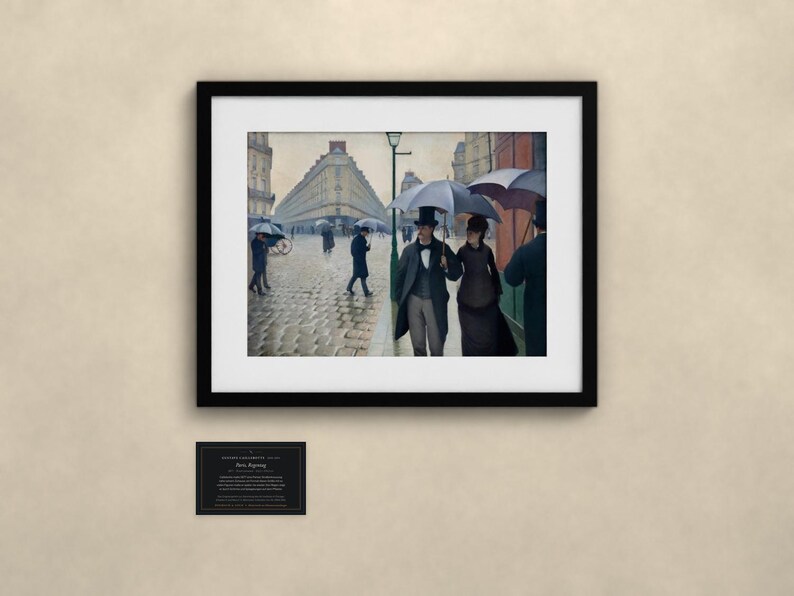May include: A framed art print depicting a rainy Paris street scene with people holding umbrellas, including a couple in the foreground. The painting features cobblestone streets, tall buildings, and a street lamp. A small informational plaque is below the frame.