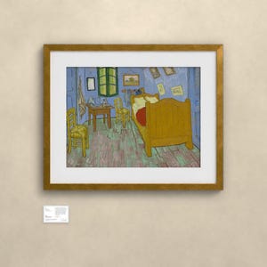 May include: A framed print of Vincent van Gogh's Bedroom in Arles painting, featuring a yellow bed, two wooden chairs, and a small table inside a blue-walled room with a green window, displayed in a gold frame with a white mat and a small label.