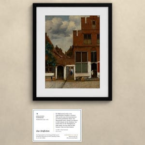 May include: A framed print of Johannes Vermeer's painting The Little Street, depicting a red brick house with a cobblestone alleyway under a cloudy sky. Below the frame is an informational card with text about the artwork and artist.