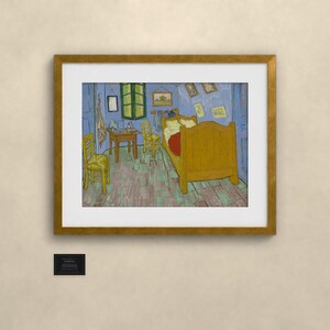 May include: A framed print of Vincent van Gogh's Bedroom in Arles painting, featuring a yellow bed, two yellow chairs, and a small table in a blue room with a green window, enclosed in a gold-colored frame with a white mat and a small black plaque.