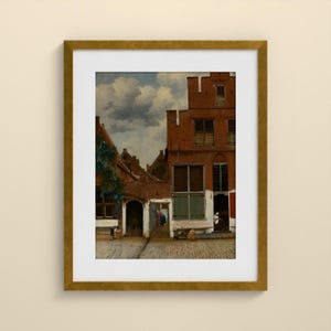 May include: A framed art print depicting a Dutch cityscape with red brick buildings, a cobblestone courtyard, and a cloudy sky. The scene features architectural details like multi-paned windows and arched doorways, presented in a gold-toned frame.