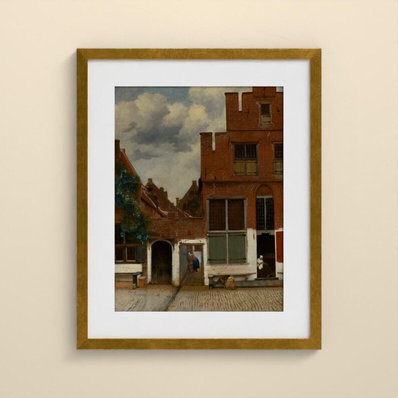 May include: A framed art print depicting a Dutch cityscape with red brick buildings, a cobblestone courtyard, and a cloudy sky. The scene features architectural details like multi-paned windows and arched doorways, presented in a gold-toned frame.
