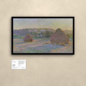 May include: A framed landscape painting depicting two haystacks in a field at sunset, with soft purple and gold light casting long shadows. The artwork is signed Claude Monet 91 in the bottom left corner. A small informational placard is below.
