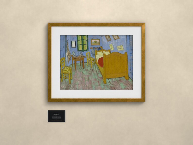 May include: A framed print of Vincent van Gogh's Bedroom in Arles painting, featuring a yellow bed, two yellow chairs, a wooden table, and blue walls, enclosed in a gold-colored frame with a small black informational plaque below it.