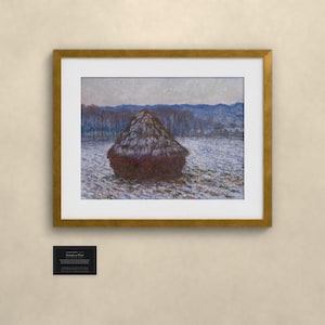 May include: A framed print of an impressionist painting featuring a dark brown haystack in a snow-covered field under a pale sky. The artwork is enclosed in a gold-colored frame with a white mat. A small black plaque with white text is below.